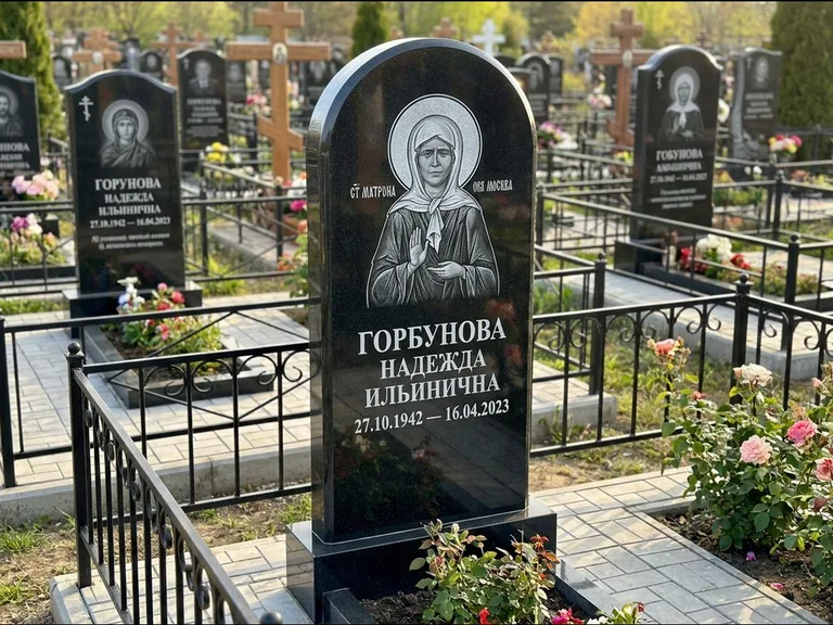Памятник с гравировкой иконы: стела с арочным верхом и киотом под образ — гравировка образа Матроны Московской, гранитный цоколь с тёмной плиткой, работа «Ковалёв» во Владивостоке