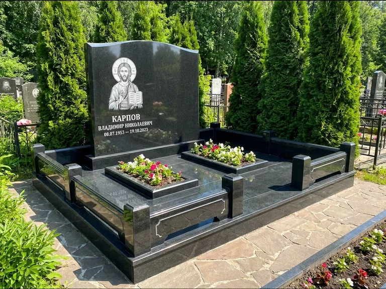 Памятник с гравировкой иконы: широкая панорамная стела с золочёным нимбом — гравировка образа Матроны Московской, цветник с белыми хризантемами, работа «Мельникова» во Владивостоке