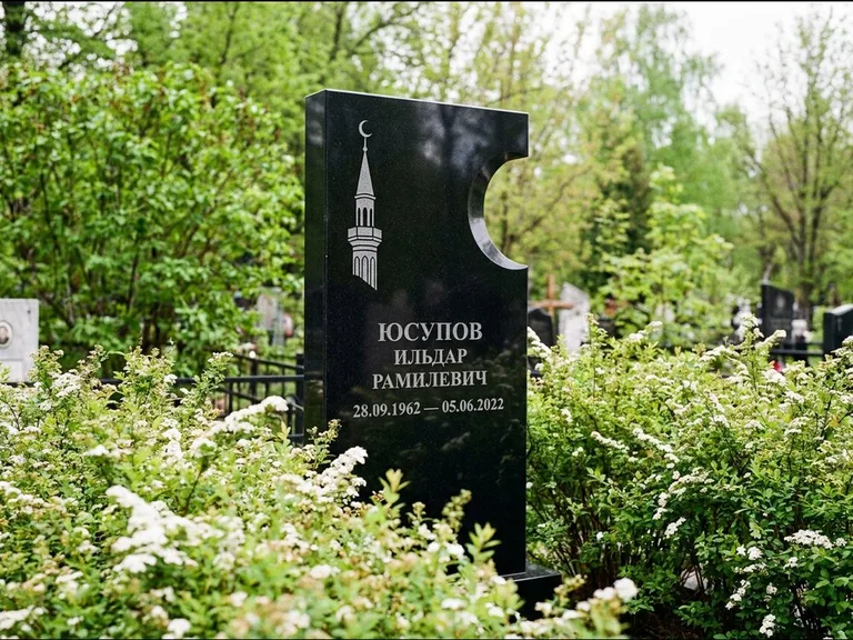 Мусульманский памятник с гравировкой мечети: стела с боковым вырезом в форме полумесяца — гравировка минарета с полумесяцем, низкие кусты спиреи в цвету, работа «Юсупов» во Владивостоке